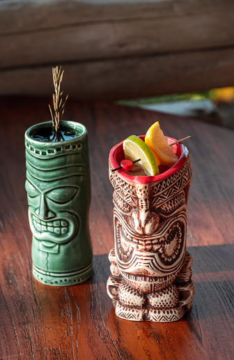 Two Tiki Cocktails mugs with fruit garnish in tropical rum bar